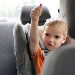 a child in a car seat giving a thumbs up